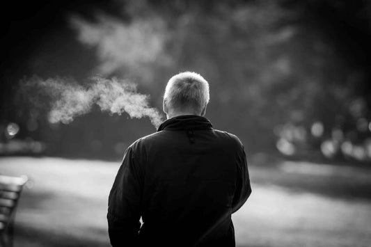 Person exhaling smoke while discussing Nicotine Pouches and Other NRTs in a park setting.