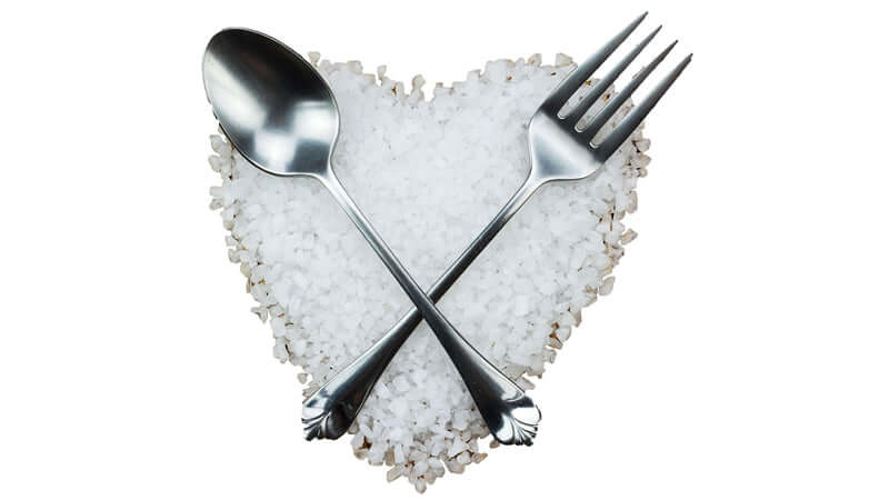 Silver fork and spoon crossed over heart-shaped sea salt, symbolizing the Role of Sodium in Your Body.