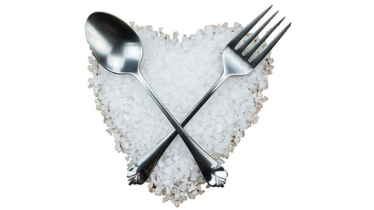 Silver fork and spoon crossed over heart-shaped sea salt, symbolizing the Role of Sodium in Your Body.