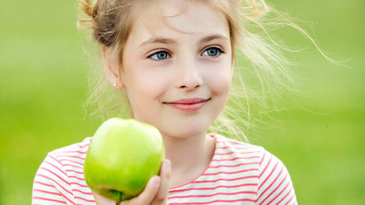 A happy girl holding a green apple, representing the phrase 'Kids They Are What They Eat'.