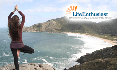 Woman practicing Yoga on a cliff overlooking the ocean with mountains in the background.