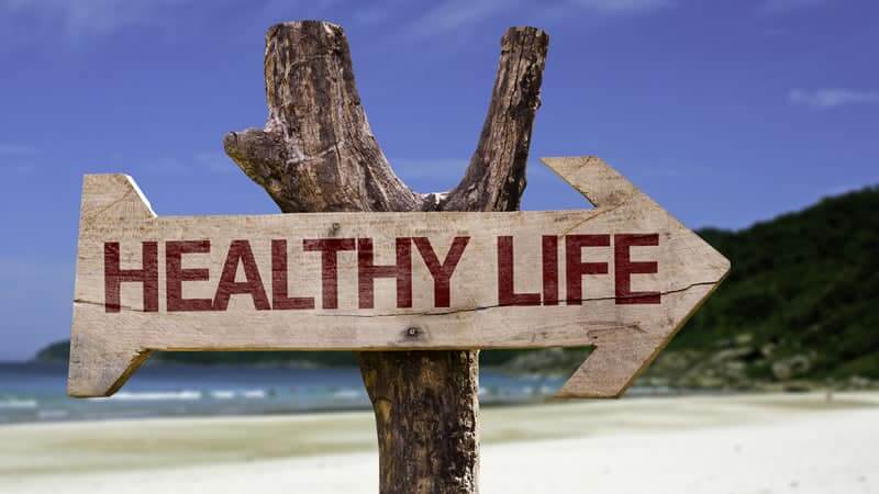 Wooden sign pointing to a direction labeled 'HEALTHY LIFE' on a beach with a clear blue sky.