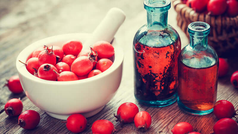 Hawthorn Berry in a white bowl with herbal tinctures in glass bottles on a wooden background.
