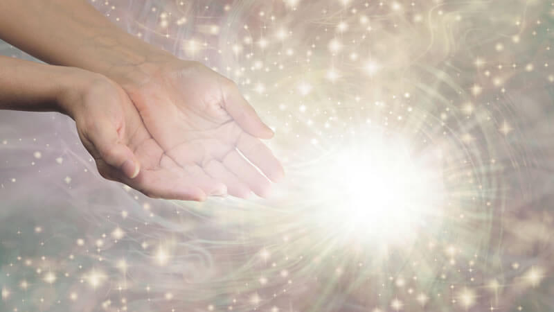 Hands reaching out with glowing energy illustrating the concept of Vibrational Medicine.