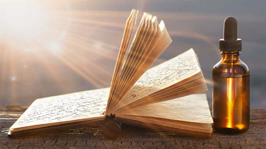 A bottle of ORMUS Oils and Lotions beside an open book, illuminated by sunlight.