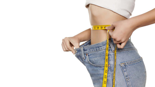 Woman measuring waist with tape while wearing oversized jeans, highlighting challenges of Weight Loss.