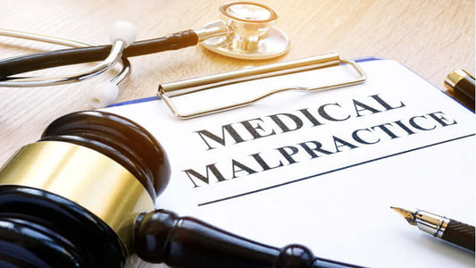 Gavel, stethoscope, and clipboard with text 'MEDICAL MALPRACTICE' on a desk.