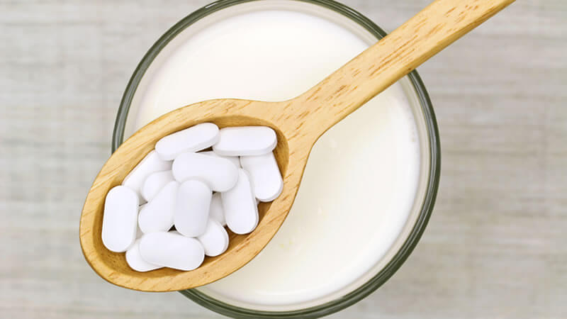 A wooden spoon holding white tablets above a glass of liquid, related to Miracle Mineral Solution.