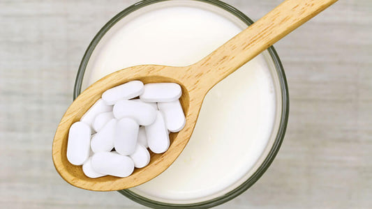 A wooden spoon with white pills over a glass of milk representing Probiotics Enzymes and Minerals.
