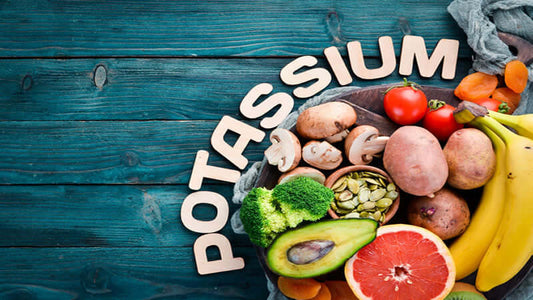 Colorful assortment of fruits and vegetables surrounding the word Potassium on a wooden table.