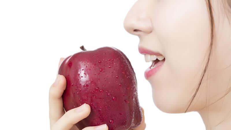 A woman holding a red apple close to her mouth, illustrating the concept of Universal Diet for Everybody.