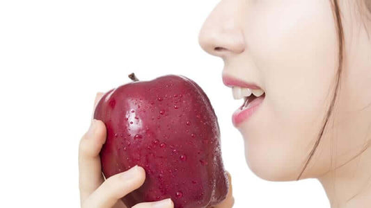 A woman holding a red apple close to her mouth, illustrating the concept of Universal Diet for Everybody.