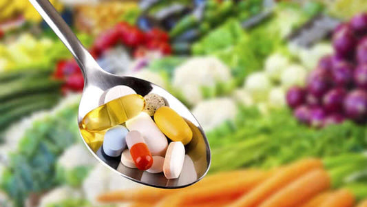 Spoonful of various pills and vitamins with fresh vegetables in the background, illustrating Nutraceuticals or Pharmaceuticals.