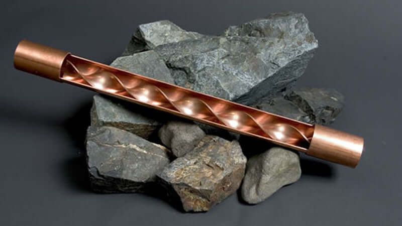 Vortex Water Energizing copper device placed on rocks, showcasing its unique spiral design for energizing water.