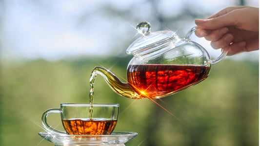 Teapot pouring tea into a glass cup, representing tea drinking customs.