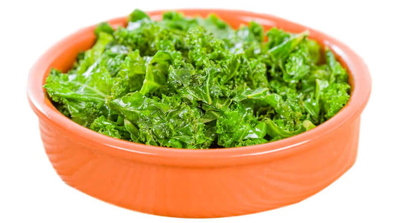 Freshly washed Kale in a vibrant orange bowl, showcasing its rich green color and texture.
