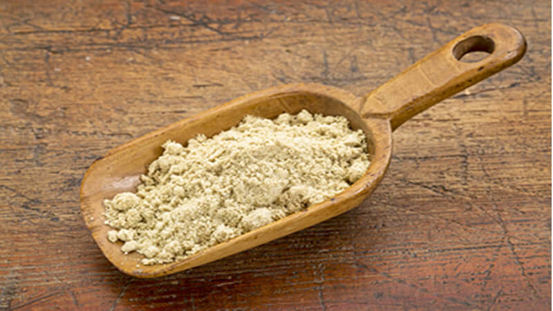 A wooden scoop filled with Rice Bran powder on a rustic wooden surface.