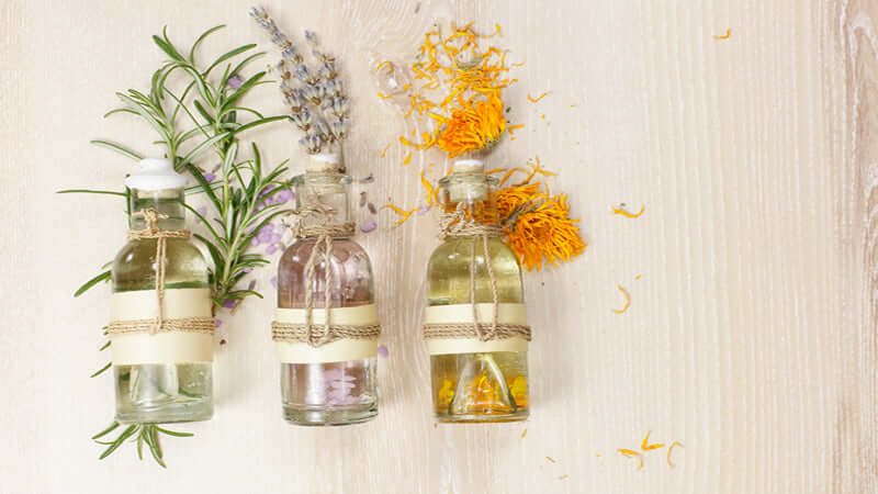 Three bottles of essential oil blends with herbs and flowers on a wooden surface.