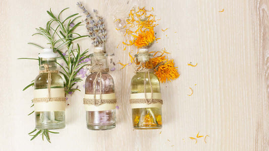 Three bottles of essential oil blends with herbs and flowers on a wooden surface.