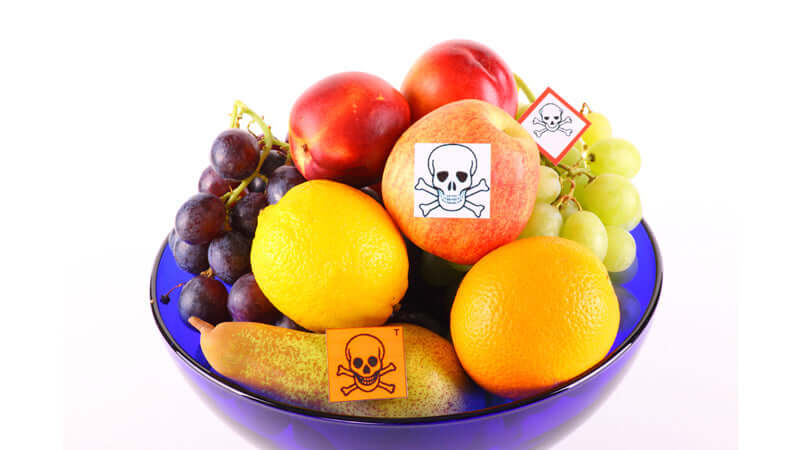 A bowl of fruits with warning labels, highlighting concerns related to food irradiation.