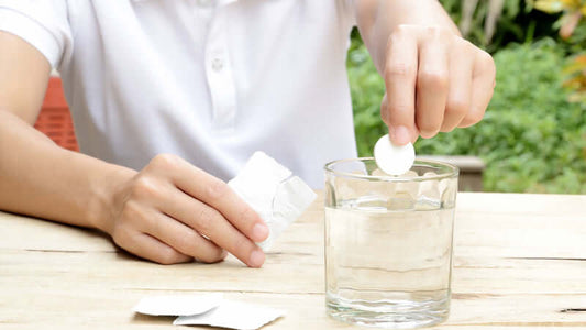 Person dropping an antacid tablet into a glass of water related to Antacid Myth.