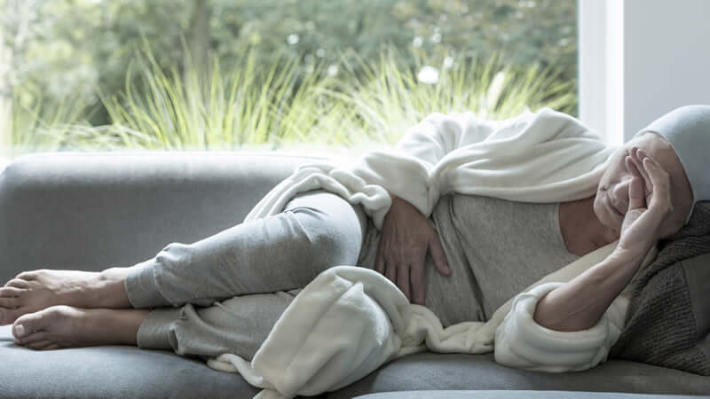 A person resting on a couch with a pained expression, representing discomfort or illness.
