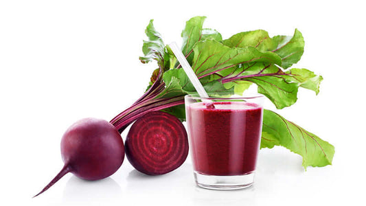 Fresh beets with a glass of beet juice and beet greens on a white background.