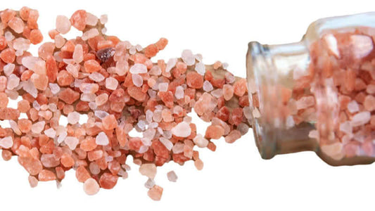 Bamboo Salt spilling from a glass jar showcasing its pink and reddish crystals.