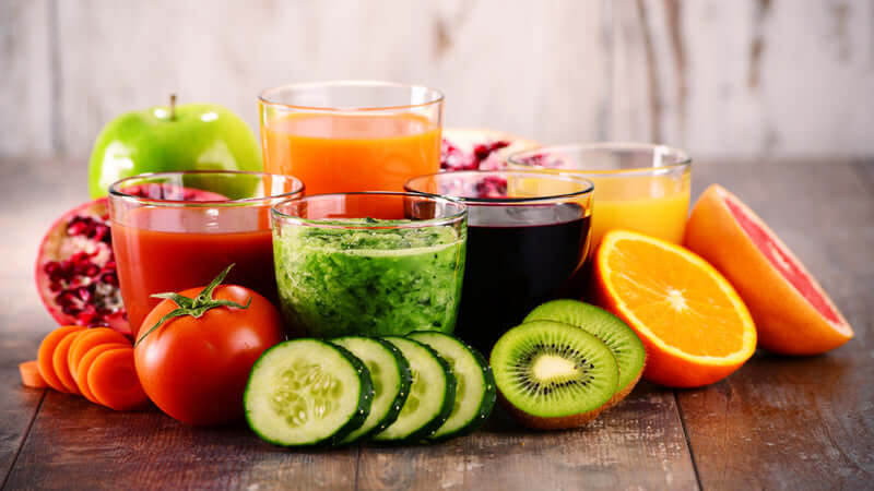 Colorful array of superfood blends in glasses with fresh fruits and vegetables on a wooden table.