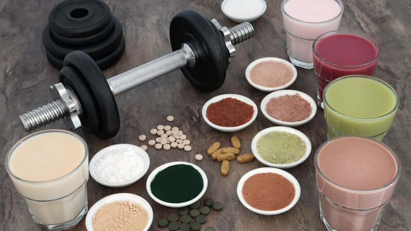 Amino Acids supplements with dumbbells and various protein shakes on a table.