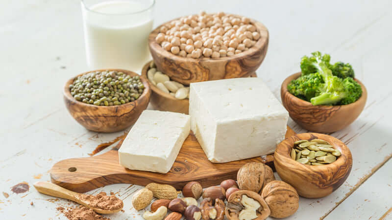 Soy Tragedy and Hype image featuring tofu, legumes, nuts, and greens on a rustic wooden table.