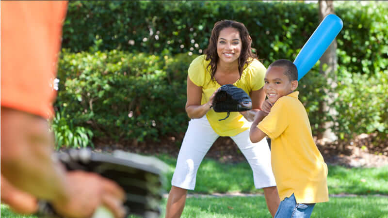 A mother and son playing baseball in the park, promoting magnesium for youth and health through active play.