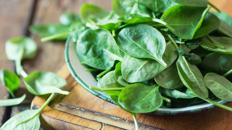 Fresh spinach leaves in a bowl on a wooden table.