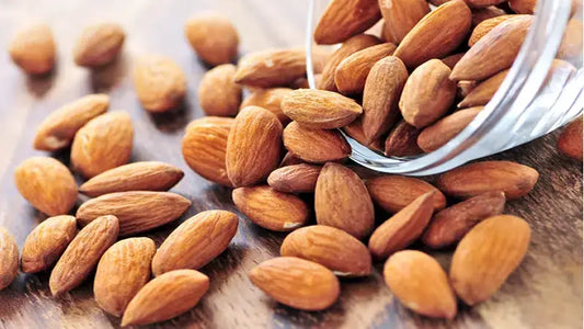 Almonds scattered from a glass jar on a wooden surface, showcasing their natural texture and color.
