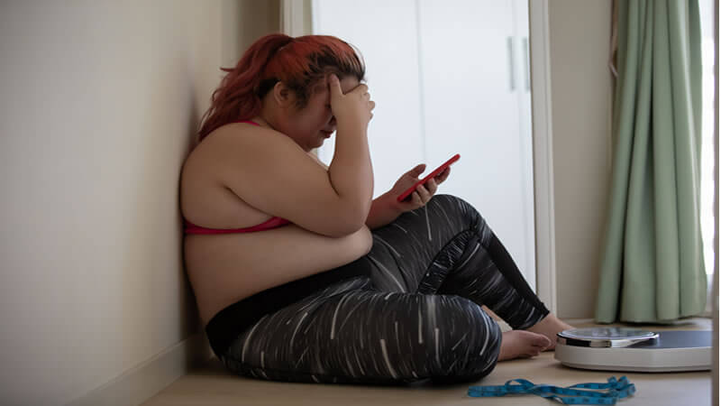 A person sitting against a wall, checking their phone in frustration, reflecting struggles related to The Body Type Diet.