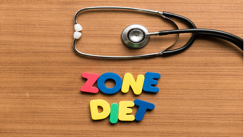 Colorful letters spelling 'ZONE DIET' next to a stethoscope on a wooden surface.