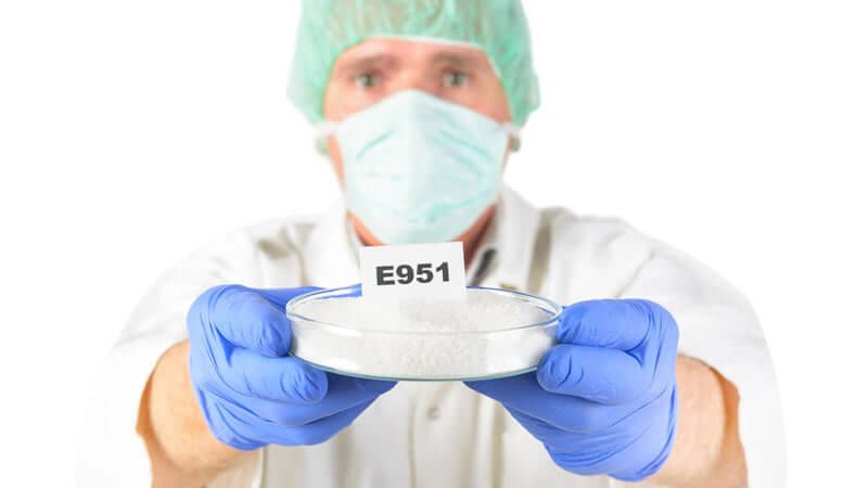 Scientist presenting E951 aspartame in a petri dish, discussing aspartame toxicity in the lab.