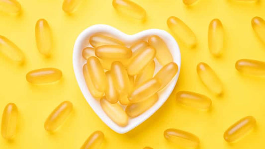 Essential Fatty Acids Explained: Heart-shaped dish with softgel capsules on a vibrant yellow background.