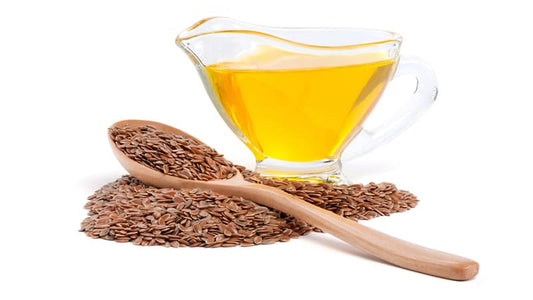 Flax Seeds and Oil in a glass container with seeds on a wooden spoon for health benefits.