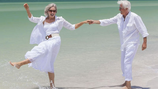 Health Basics to Enjoy a Pain-free Life: Happy senior couple enjoying life at the beach in white outfits.