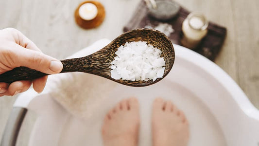 Person holding spoon of Epsom salt for magnesium treatments in foot bath.