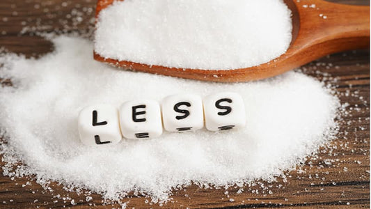 Wooden spoon with sugar and dice spelling 'LESS' to emphasize reducing sugar intake.