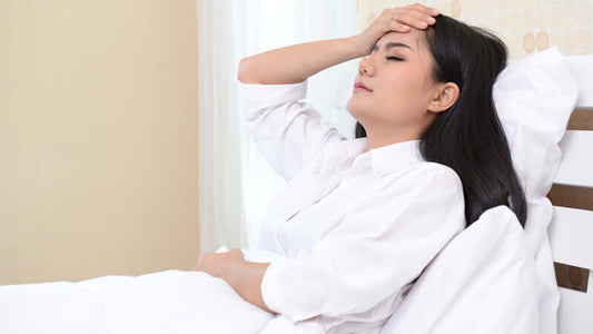 Woman lying in bed with headache, showing discomfort related to magnesium deficiency and health.