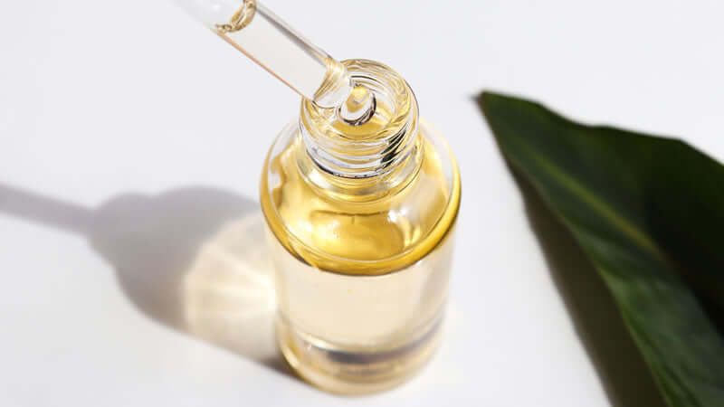 Ratite Oil Research - Close-up of a clear dropper bottle with golden oil and green leaf background.
