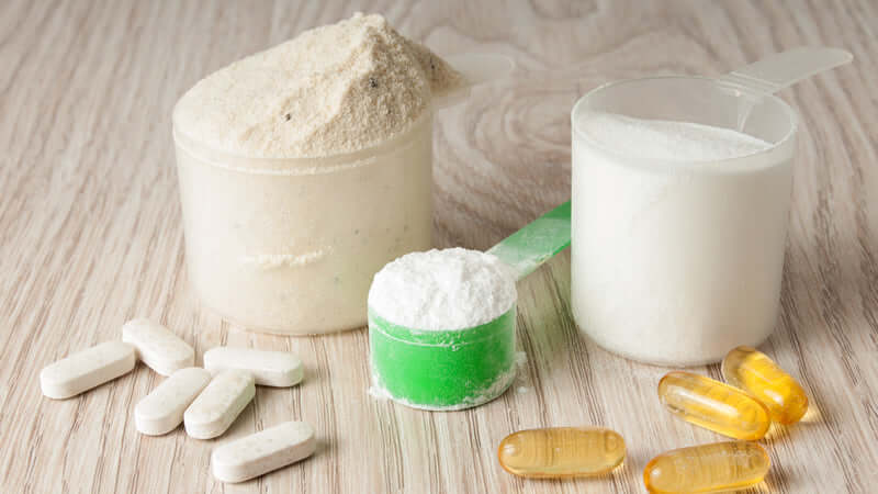 Amino Acids supplements in various forms including powder, capsules, and tablets on a wooden surface.