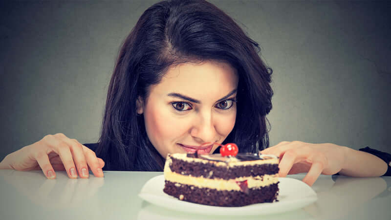 A woman experiencing food cravings while looking at a delicious chocolate cake.