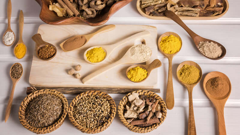 Various herbs and spices on a wooden table highlighting the debate between Herbs or Drugs.
