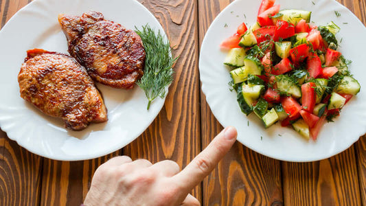 A hand pointing at a plate of salad while meat is on the other plate, illustrating Vegan Against Meat.