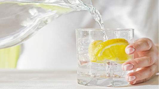 Hydration Research: A hand pouring water with lemon into a glass, emphasizing the importance of hydration.