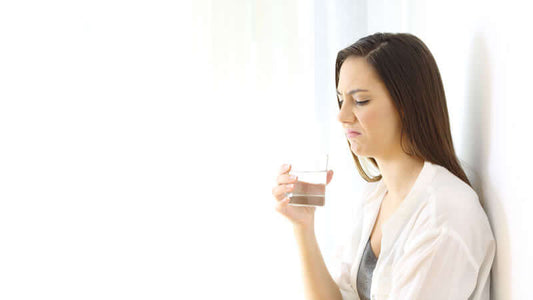 Woman grimacing while holding a glass of chloraminated water, questioning its taste.